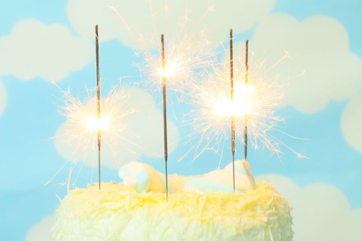 Bolo branco com quatro velas chama estrelar em cima do bolo. As velas são um produto Bello Festas.